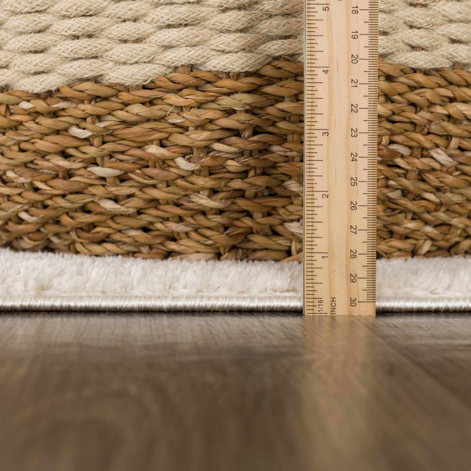 Close up of the Keone Ivory Area Rug showing the beige woven texture and pile height with a ruler. Pile
