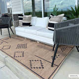 Outdoor patio scene with a camel Fathi Washable Area Rug, white sofa, and gray chairs. The rug has a geometric dark brown pattern. Roomscene-Rectangle