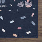 Close-up of the Milne Navy Dinosaur Washable Kids Rug, featuring a navy background with dinosaur shapes and colorful confetti accents. Corner