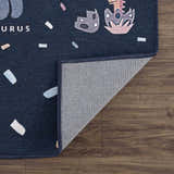 Close-up of the Milne Navy Dinosaur Washable Kids Rug showing its navy blue color, dinosaur pattern, and the rug's backing. Fold