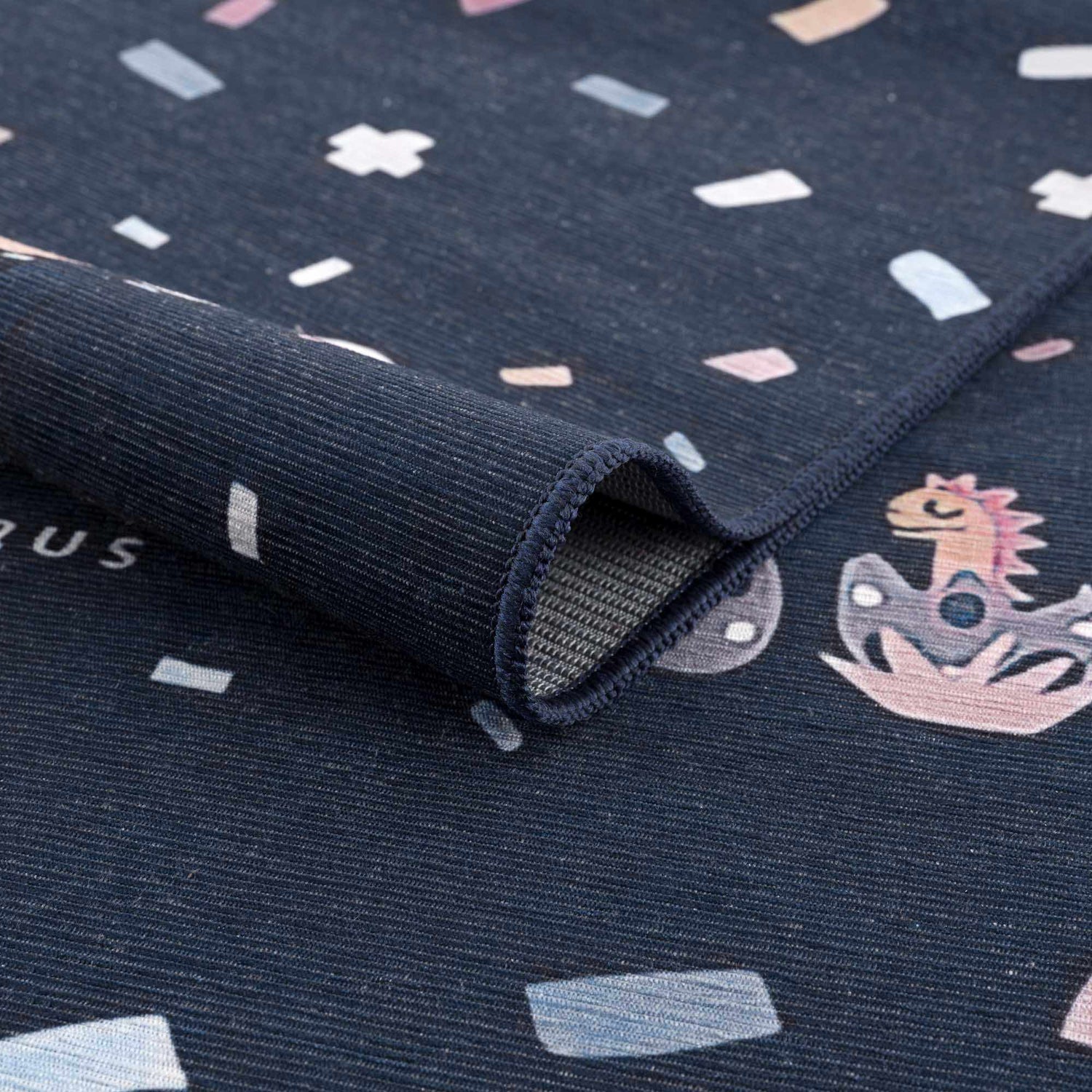 Close-up of the Milne Navy Dinosaur Washable Kids Rug, featuring a playful dinosaur pattern and a durable, textured weave. Fold