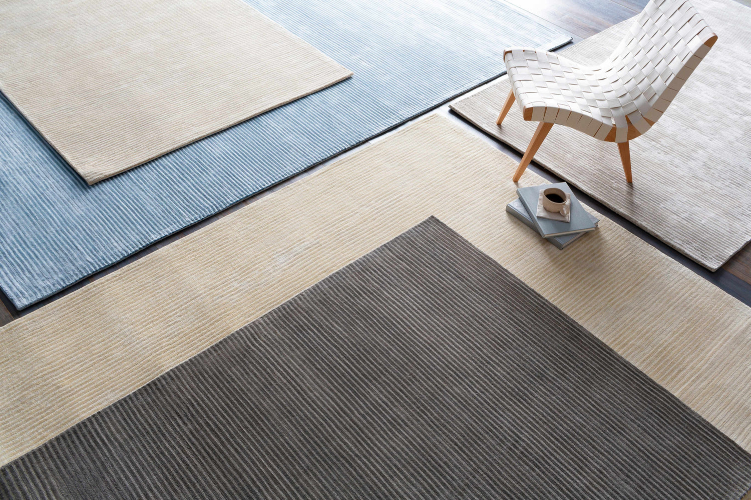 Overhead view of Ahmeek Area Rug samples in gray, beige, and blue with linear texture, styled with a chair and coffee. Styleshot