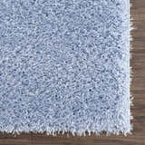 Close-up of the Faina Solid Aqua Shag Washable Area Rug showing its plush texture and light blue color against a wood floor. Swatch