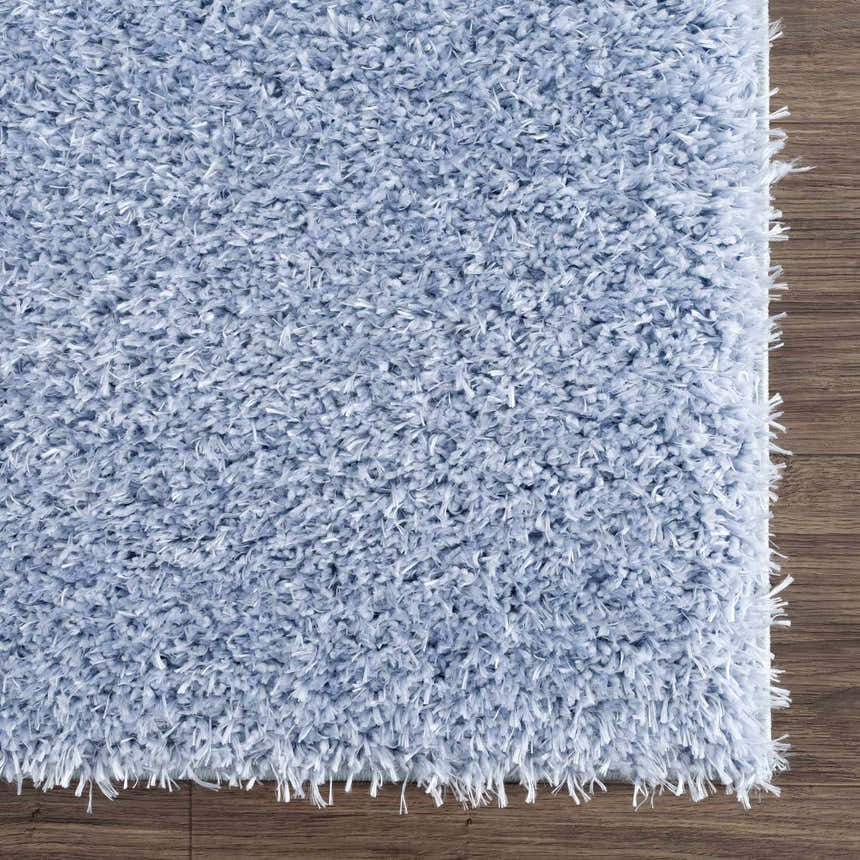 Close-up of the Faina Solid Aqua Shag Washable Area Rug showing its plush texture and light blue color against a wood floor. Swatch