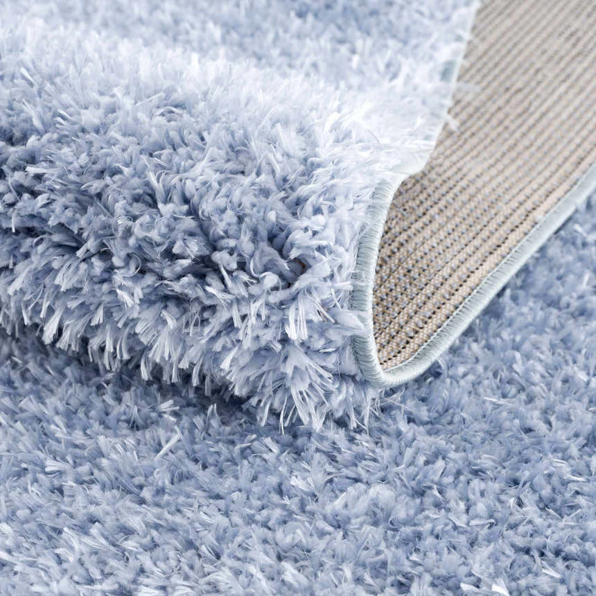 Close-up of the plush texture and backing of the Faina Solid Aqua Shag Washable Area Rug. Fold