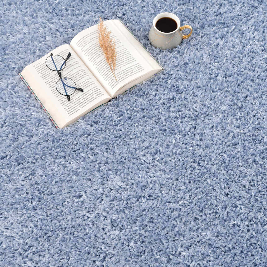 Aqua Faina Solid Shag Rug close-up. Soft, plush texture with a book, coffee, and glasses on top. Perfect for a cozy room. Styleshot