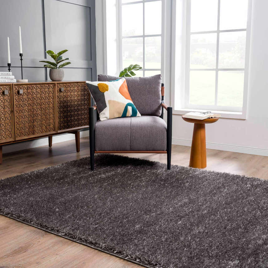 Living room scene with a Faina Solid Dark Gray Shag Washable Area Rug, gray chair, wood cabinet, and light wood floors. Roomscene-Rectangle