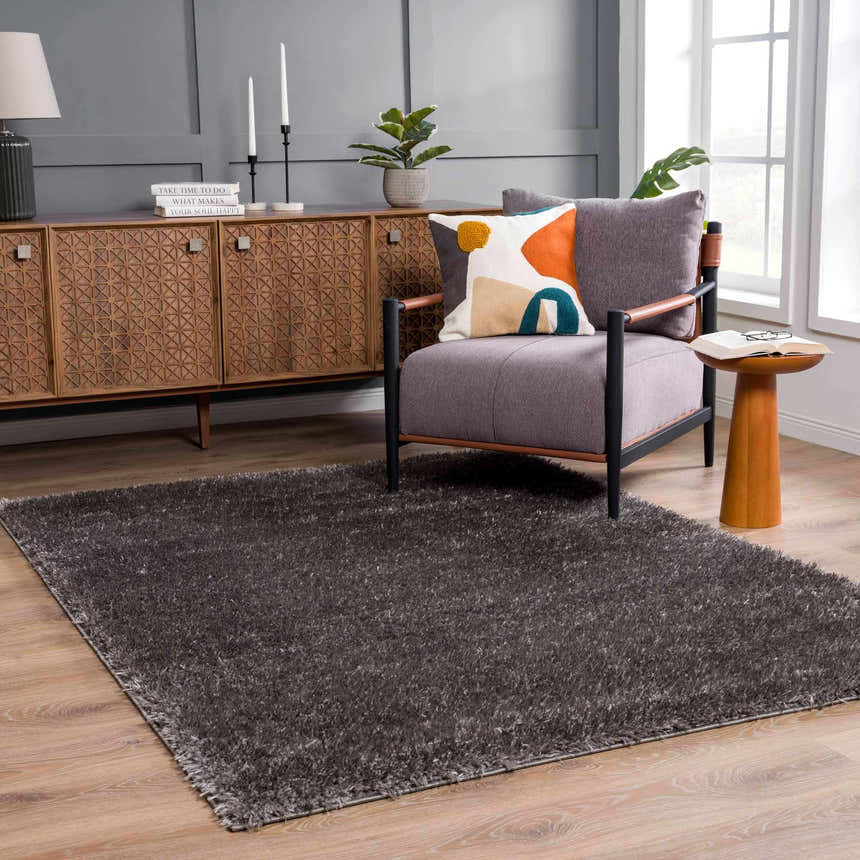Living room scene with Faina Solid Dark Gray Shag rug, gray chair with colorful pillow, and wood accent furniture. Roomscene-Rectangle