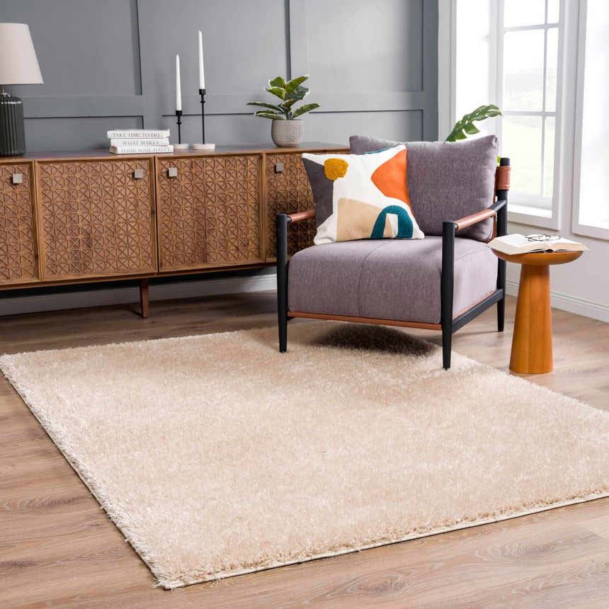 Living room scene with Faina Solid Beige Shag Washable Area Rug, gray walls, wood furniture, and a comfortable chair. Roomscene-Rectangle