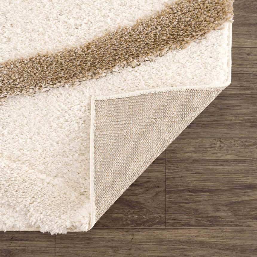 Close-up of the Espiye Area Rug showing the driftwood stripe, off-white shag texture, and backing on a dark wood floor. Fold