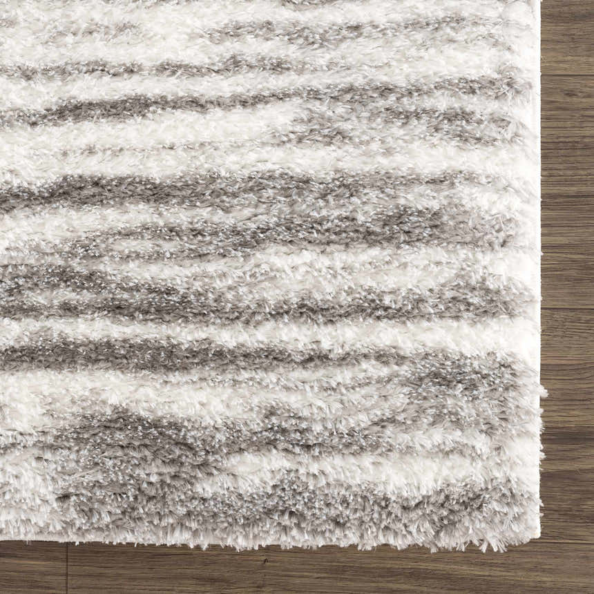 Close-up of the Lotta Area Rug. Gray and white shag rug with a horizontal stripe pattern on a wood floor. Swatch