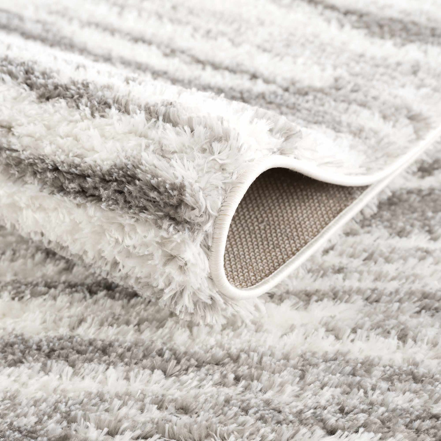Close-up of the Lotta Area Rug, a shag rug in gray and white stripes. Shows texture and backing. Fold