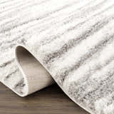 Close-up of the Lotta Area Rug, a gray and white shag with a striped pattern, showing the rug's texture and backing. Fold