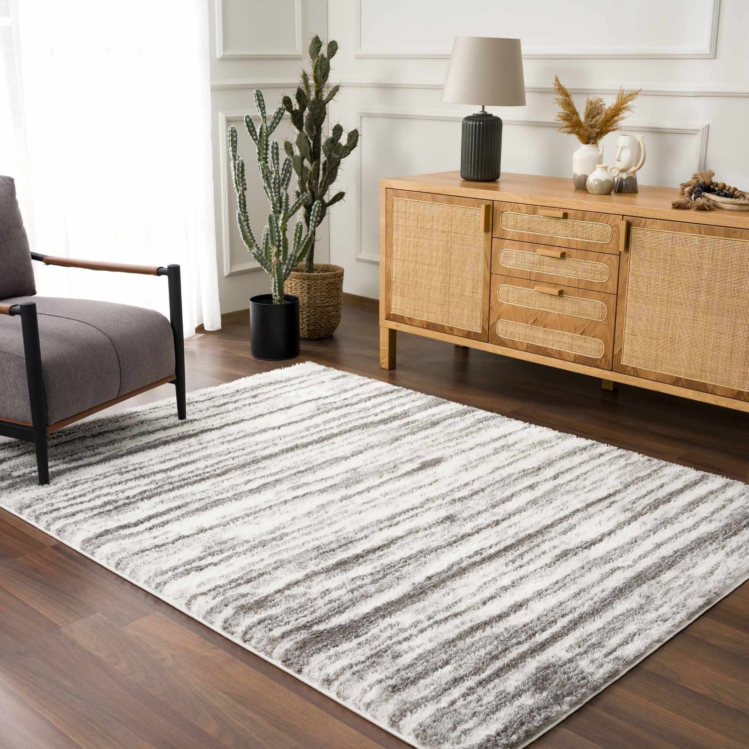 Living room scene with a gray chair and wood cabinet featuring the gray and white striped Lotta Area Rug. Roomscene-Rectangle