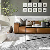 Living room scene with a gray Hedda Boutique Washable Rug, brown leather sofa, white chair, and black coffee table. Roomscene-Rectangle