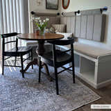 Dining room with gray Hedda Boutique Washable Rug, round wood table, black chairs, and built-in bench seating. Roomscene-Rectangle