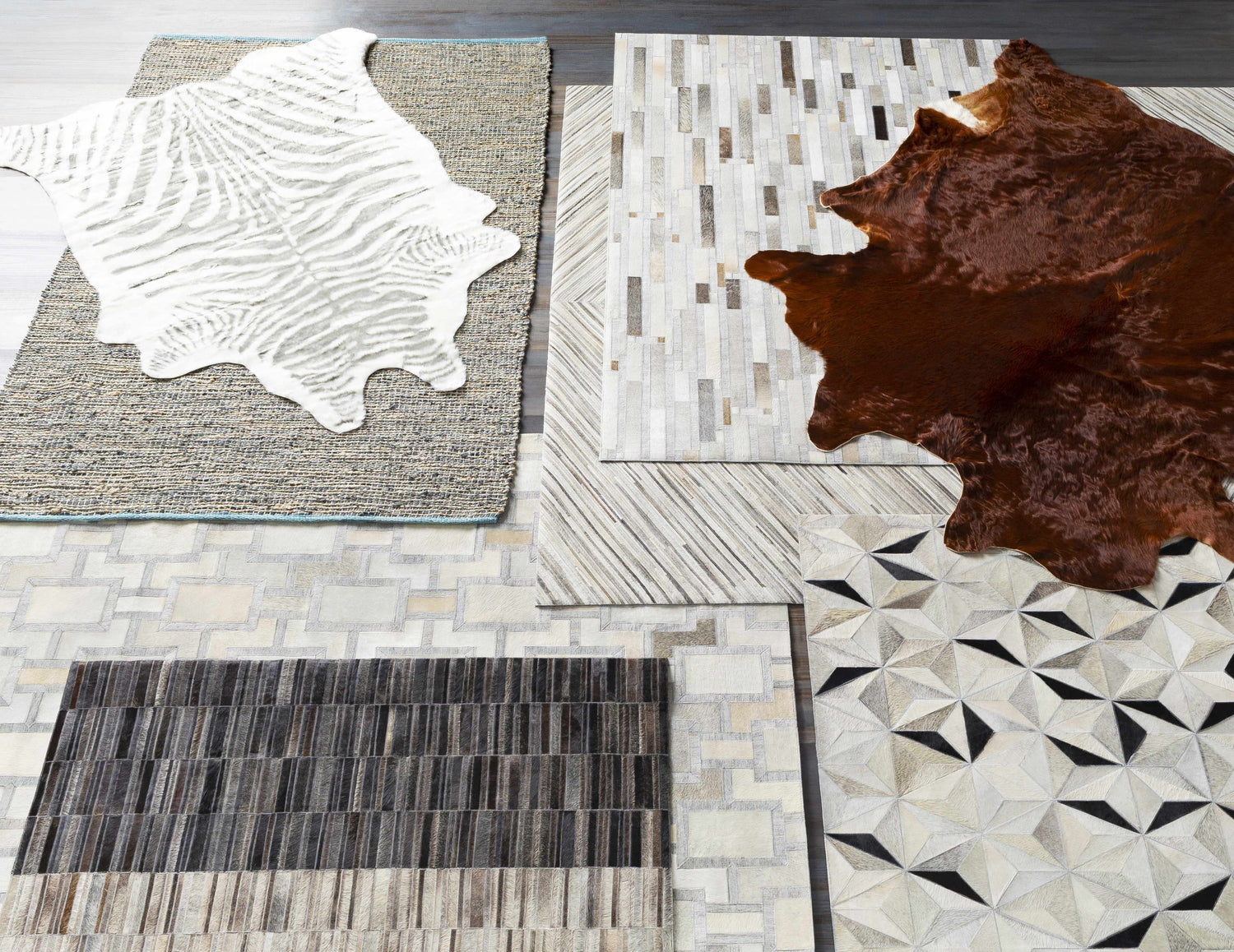 Close-up of several Wauzeka Premium Area Rugs showing animal hide, geometric, and striped designs in brown, cream, and gray tones. Styleshot