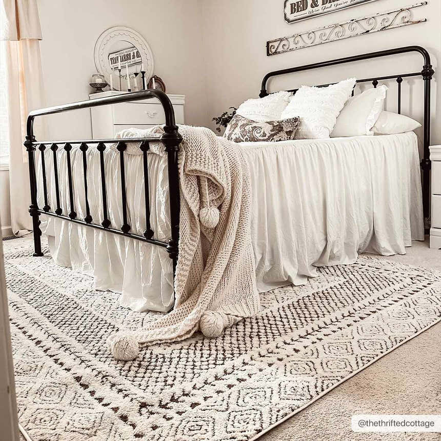 Bedroom scene with a black iron bed frame and the beige Julio Scandi Boho Area Rug. Roomscene-Rectangle