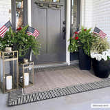 Entryway scene with a beige Kidron Area Rug featuring a black and white geometric border. Planters and lanterns decorate the porch. Roomscene-Rectangle