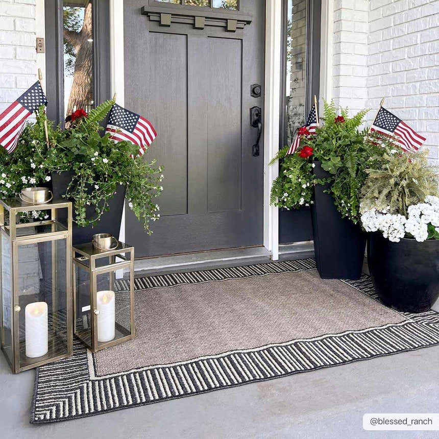 Entryway scene with a beige Kidron Area Rug featuring a black and white geometric border. Planters and lanterns decorate the porch. Roomscene-Rectangle