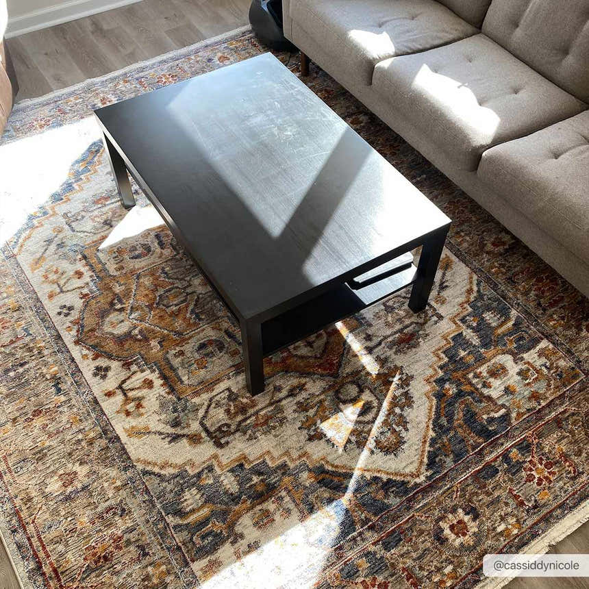 Living room scene with a Kokstad Area Rug in arctic stone, beige, brown, and blue under a black coffee table and gray sofa. Roomscene-Rectangle