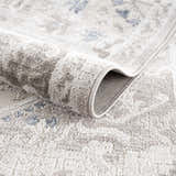 Close-up of the Bakir Area Rug showing its traditional gray and blue pattern and soft, machine-woven texture. Fold