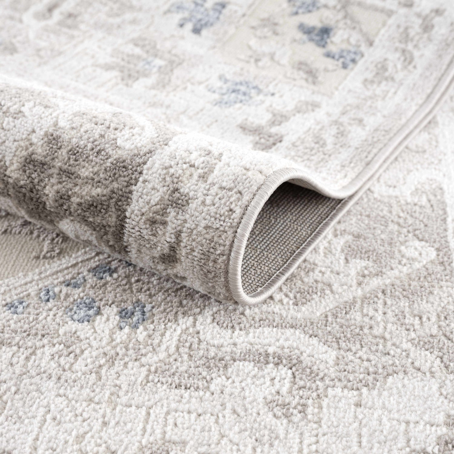 Close-up of the Bakir Area Rug showing its traditional gray and blue pattern and soft, machine-woven texture. Fold