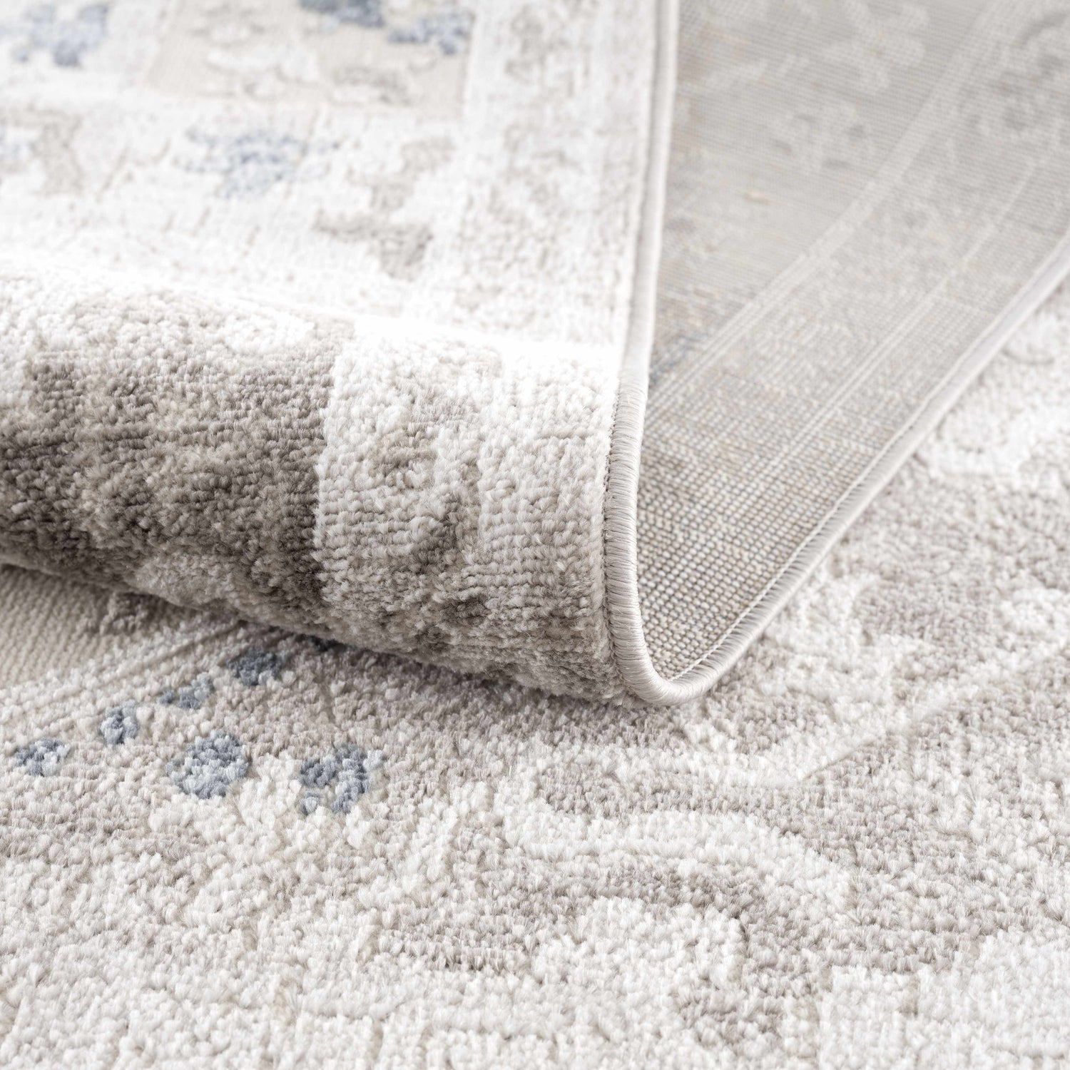Close-up of the Bakir Area Rug showing its plush texture, gray and blue traditional pattern, and machine-woven construction. Fold