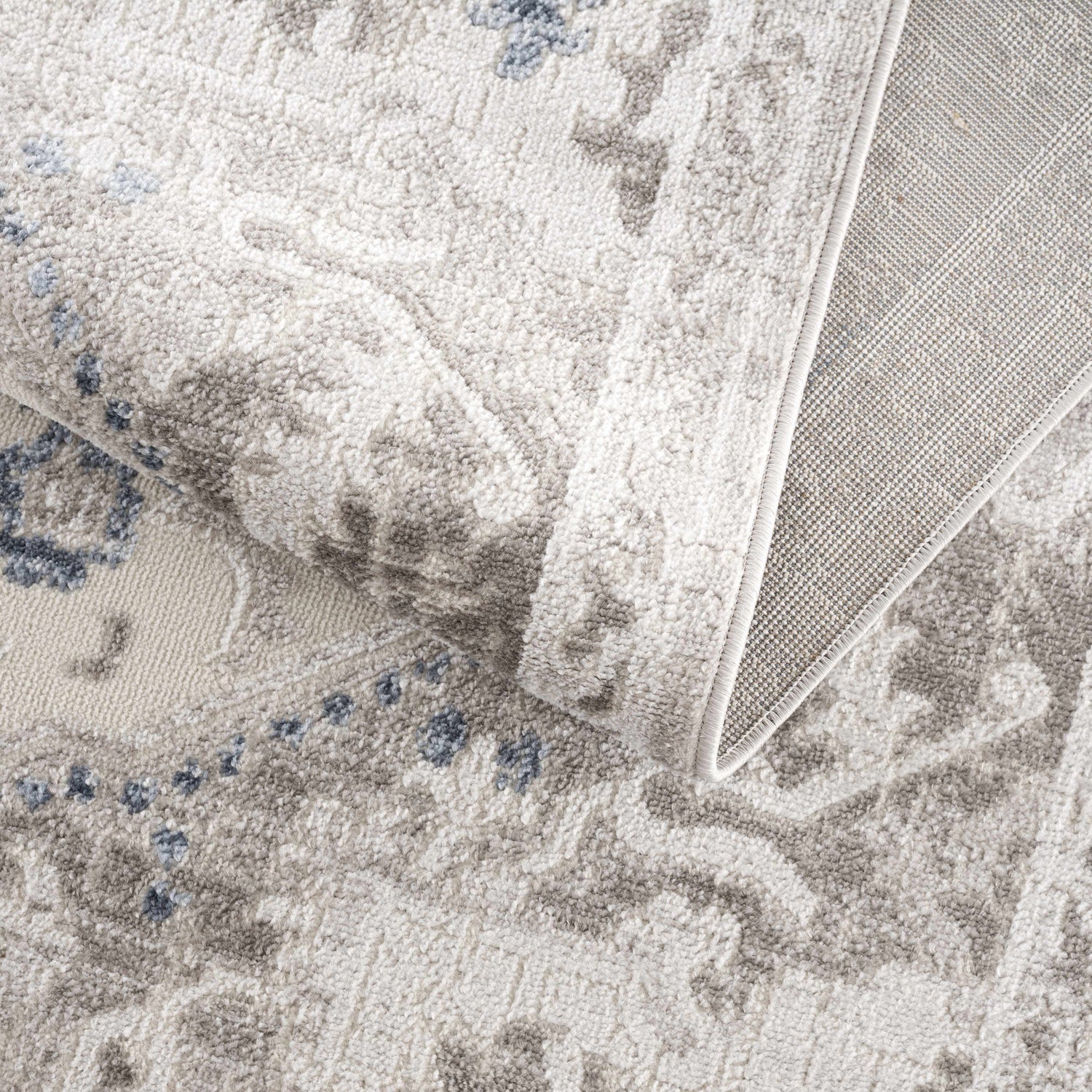 Close-up of the Bakir Area Rug. Machine woven rug in blue and gray with a traditional pattern and textured pile. Fold