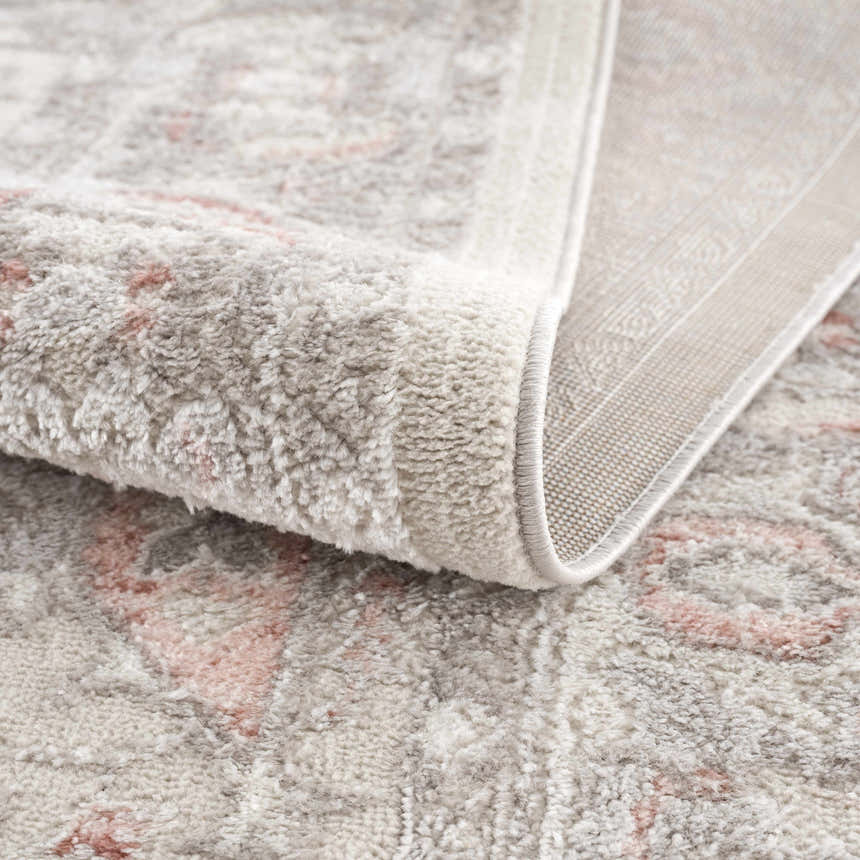 Close-up of the Damla Area Rug showing its gray and pink vintage pattern and soft, textured pile. Fold