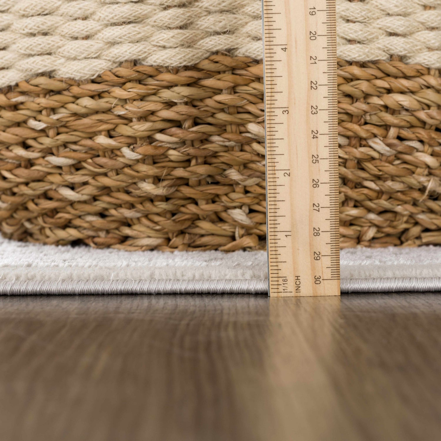 Close-up of the Damla Area Rug showing the gray and beige braided texture and pile height with a ruler. Pile