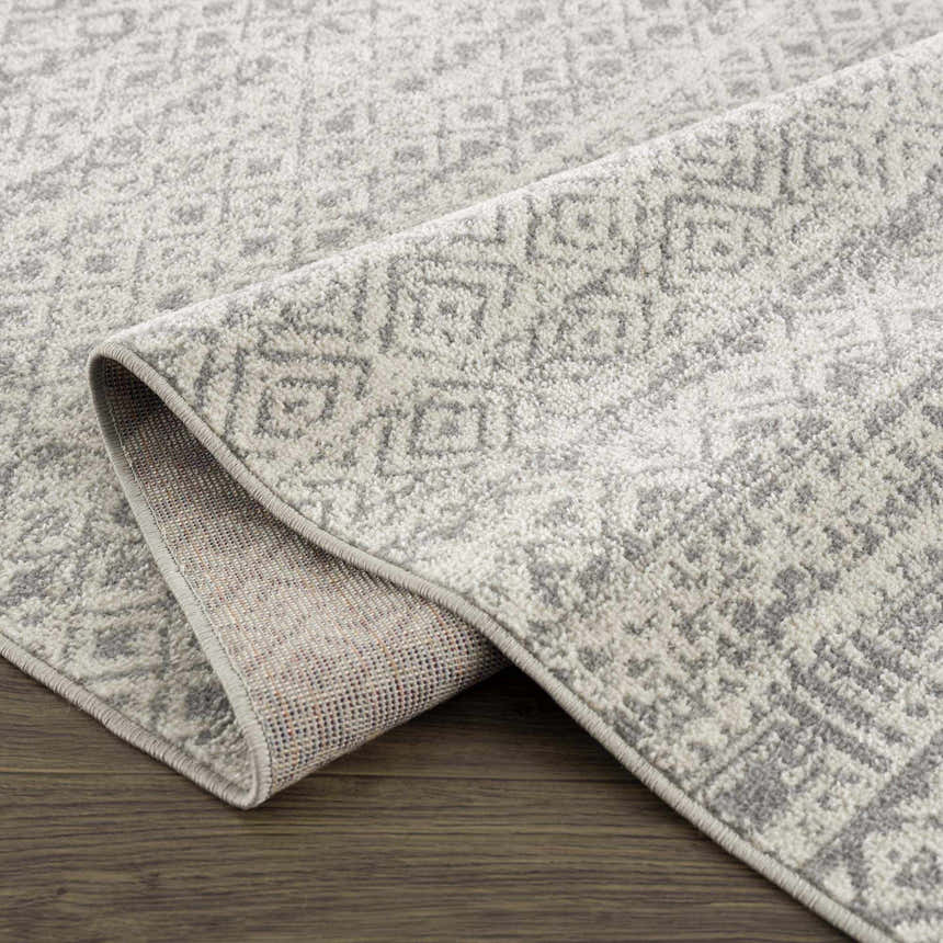 Close-up of the Gravelbourg Washable Boho Rug. Light gray and gray geometric pattern. Machine woven polyester rug. Fold