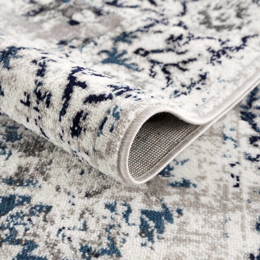 Close-up of the Duena Area Rug showing its blue and light gray traditional pattern and machine woven construction. Fold