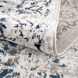 Close-up of the Duena Area Rug showing its blue and light gray traditional vintage pattern and machine woven texture. Fold