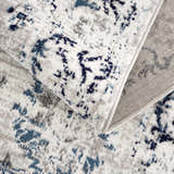 Close up of the Duena Area Rug showing its blue and light gray traditional vintage pattern and texture. Fold