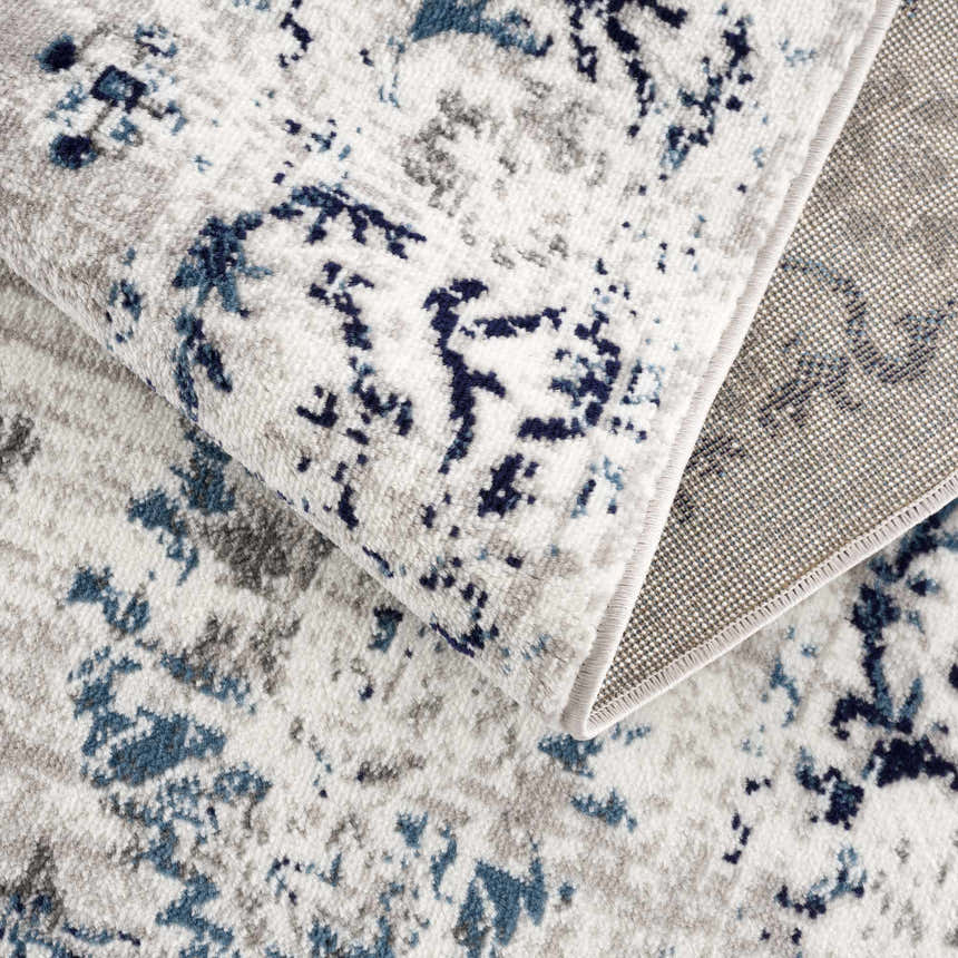 Close up of the Duena Area Rug showing its blue and light gray traditional vintage pattern and texture. Fold