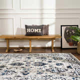 Entryway scene with blue and gray Duena Area Rug, wood bench, pillows, artwork, and houseplant. Roomscene-Rectangle
