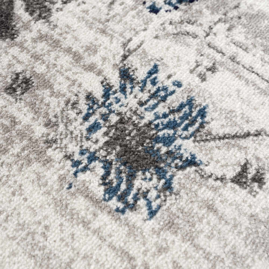 Close-up of the Duena Area Rug showing its light gray and blue traditional floral pattern and soft polypropylene texture. Texture