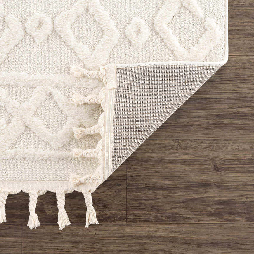 Close-up of the bone Gyundyukoru Area Rug showing geometric design, tassels, and machine woven construction on wood floor. Fold