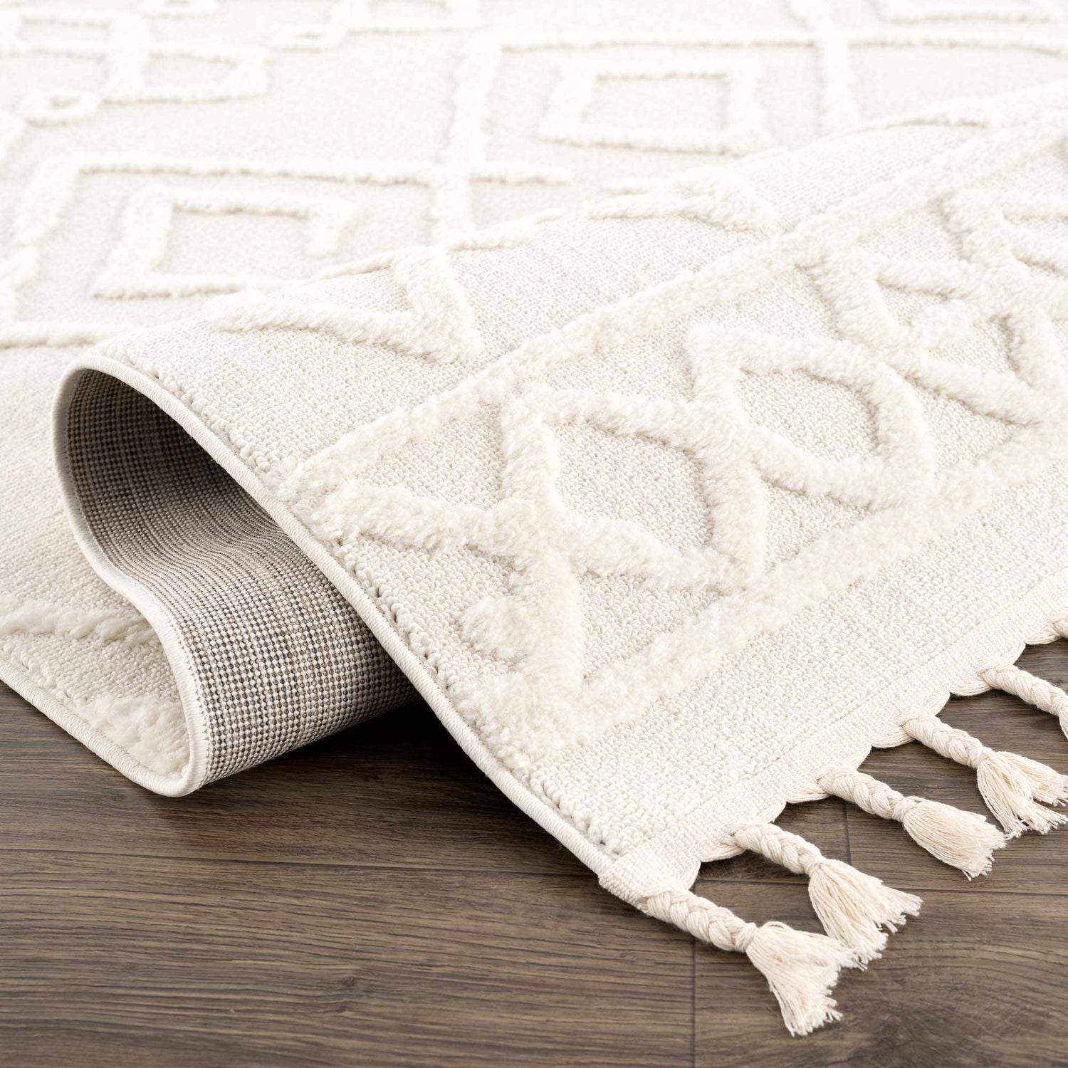 Close up of the bone Gyundyukoru Area Rug showing geometric pattern and tassels. Fold