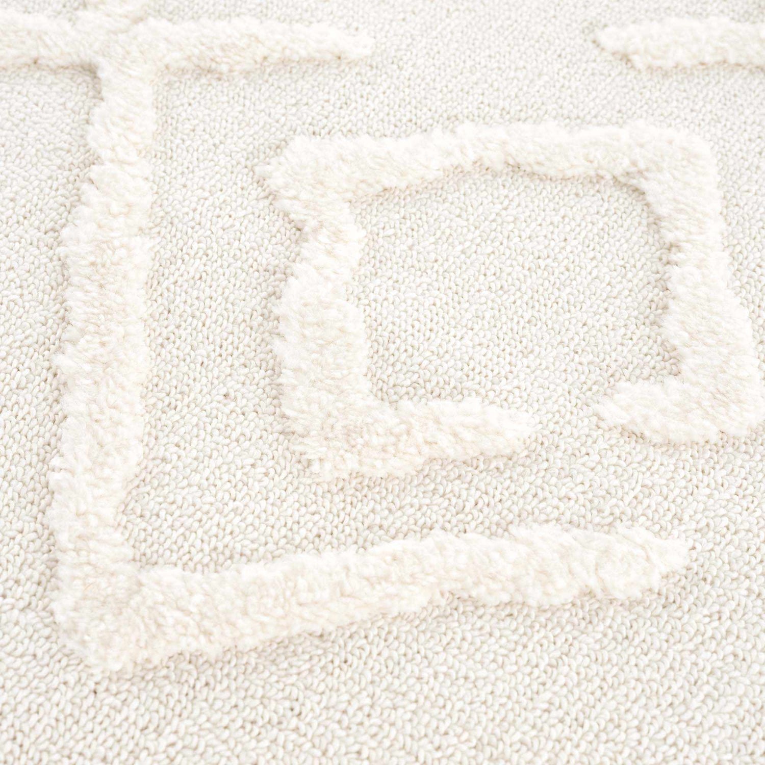 Close up of the Gyundyukoru Area Rug featuring a geometric design in bone and cream. Soft, textured polypropylene rug. Texture