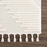 Close-up of the Palimbang Cream 3D Rug. Features a geometric pattern, plush texture, and braided tassels on a wood floor. Swatch