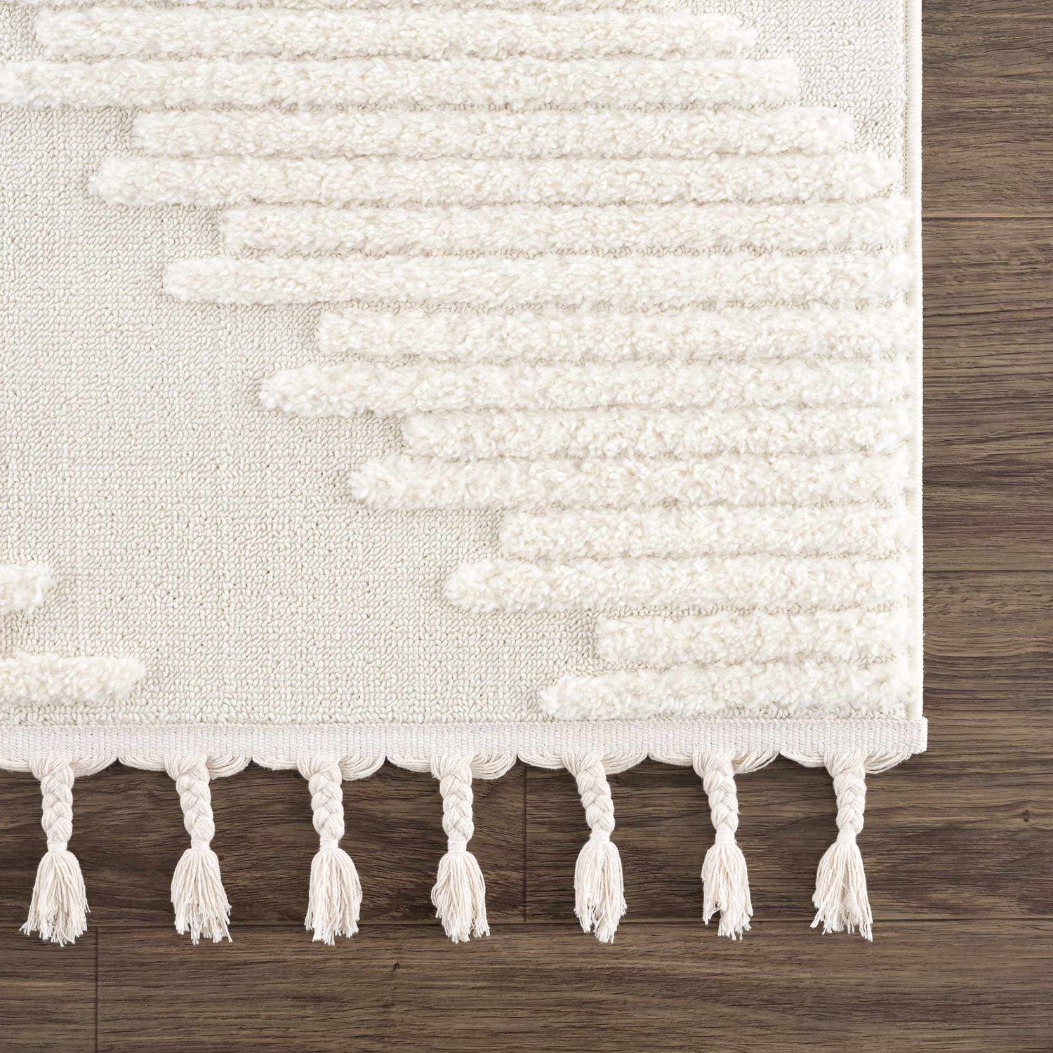 Close-up of the Palimbang Cream 3D Rug. Features a geometric pattern, plush texture, and braided tassels on a wood floor. Swatch