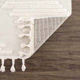 Close-up of the Palimbang Cream 3D Rug showing geometric textures, tassels, and the rug's backing on a wood floor. Fold