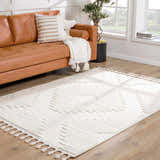 Living room scene with a tan leather sofa and the Palimbang Cream 3D Rug with geometric patterns and tassels on a wood floor. Roomscene-Rectangle