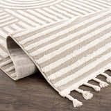 Close-up of the Moise Area Rug. Beige and cream rug with geometric and striped patterns, and decorative tassels. Fold