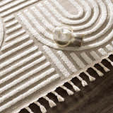 Close up of the Moise Area Rug featuring a beige background and cream geometric pattern with tassels. Styleshot