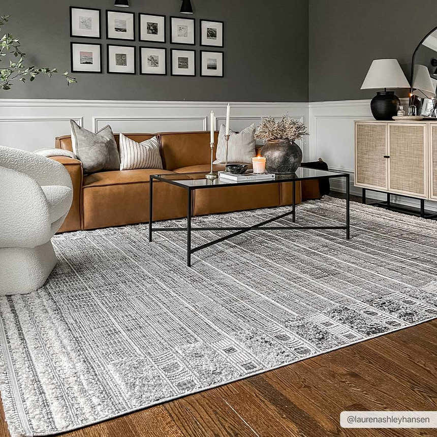 Living room scene with a charcoal wall, brown leather sofa, and Naivasha Elegant High/Low Area Rug in charcoal and cream. Roomscene-Rectangle