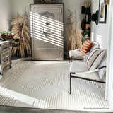 Living room scene with a Palimbang Cream 3D Rug, white chairs, a large safe, and natural decor in a bright, sunlit space. Roomscene-Rectangle