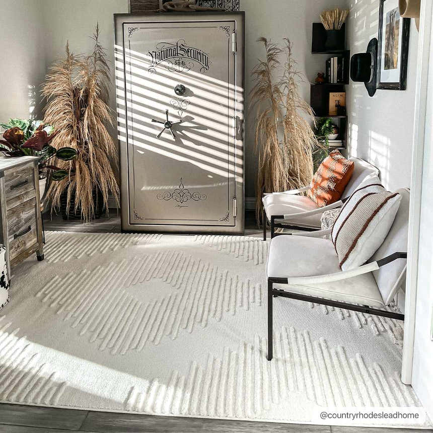 Living room scene with a Palimbang Cream 3D Rug, white chairs, a large safe, and natural decor in a bright, sunlit space. Roomscene-Rectangle